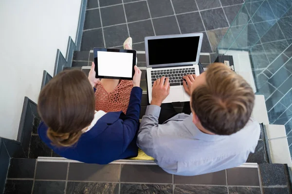 Empresario y mujer sentados en los escalones usando portátil y tableta digital —  Fotos de Stock