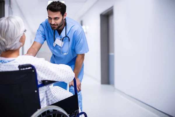 与高级病人在走廊里的轮椅上进行交互的男医生 — 图库照片