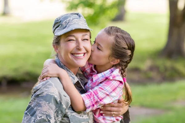 Lykkelig kvinnelig soldat som blir kysset av sin datter i parken – stockfoto