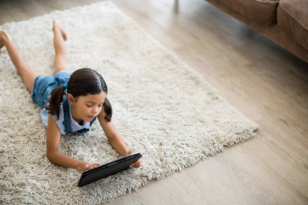 Fille à l'aide d'une tablette numérique tout en étant couché sur le tapis dans le salon — Photo