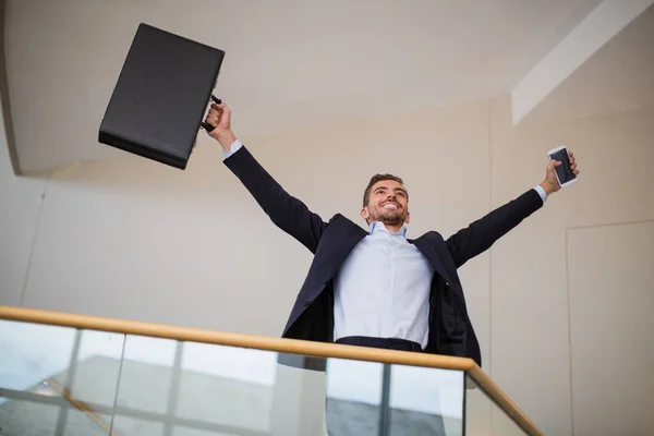 Businessman holding a briefcase and mobile phone cheering — Stock Photo, Image