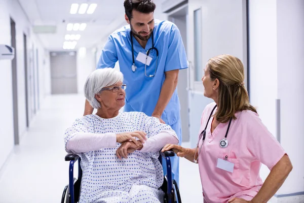 Mężczyzna i kobieta lekarz interakcji z starszy pacjentka na wózku inwalidzkim w korytarzu — Zdjęcie stockowe