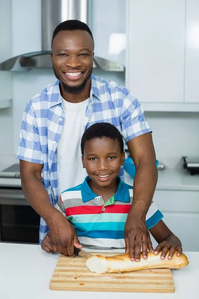 Padre ayudando a su hijo a cortar pan de pan en la cocina en casa — Foto de Stock