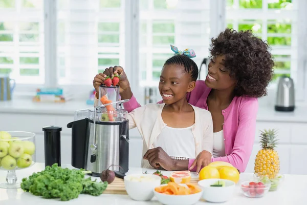 Sonriente madre e hija preparando batido de fresa en la cocina —  Fotos de Stock