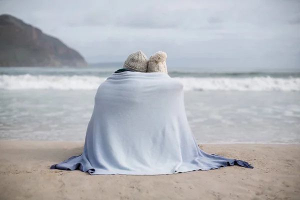 Pareja madura envuelta en manta en la playa — Foto de Stock