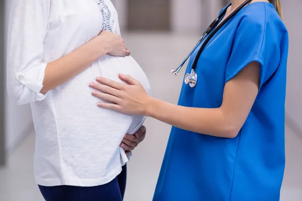 Seção média do médico tocando barriga de mulheres grávidas no corredor — Fotografia de Stock