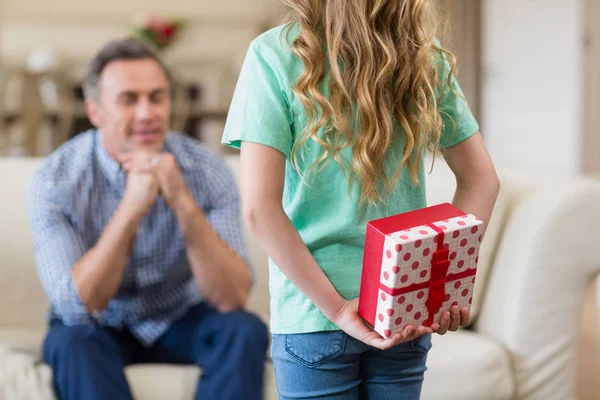 Chica sosteniendo regalo sorprendido para su padre en la sala de estar — Foto de Stock