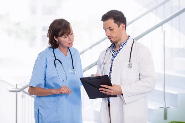 Enfermera y médico discutiendo sobre portapapeles en el pasillo — Foto de Stock