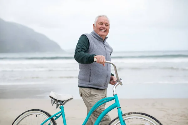 Старший мужчина, стоящий с велосипедом на пляже — стоковое фото