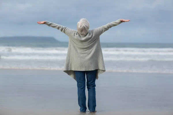 Seniorin steht mit ausgestreckten Armen am Strand — Stockfoto