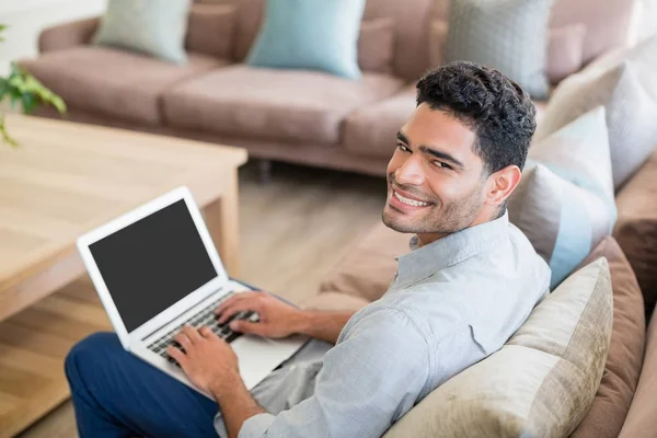 Man sitter på soffan och använder bärbar dator i vardagsrummet hemma — Stockfoto
