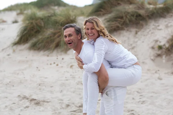 Mogen man ger piggyback rida till kvinna på stranden — Stockfoto