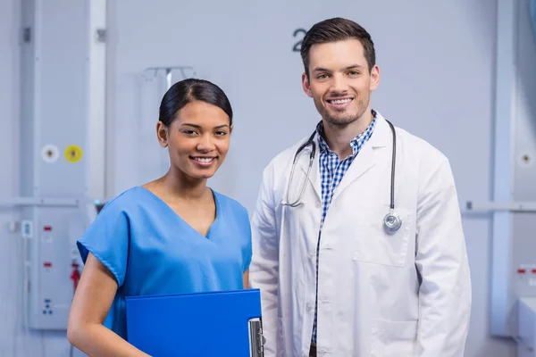 Retrato del médico sonriente y la enfermera de pie con portapapeles — Foto de Stock