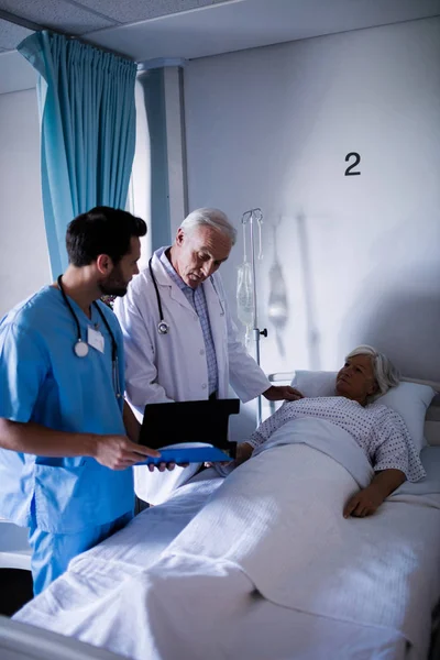 Lekarze, omawiając zaświadczenie lekarskie z pacjentem na łóżku — Zdjęcie stockowe