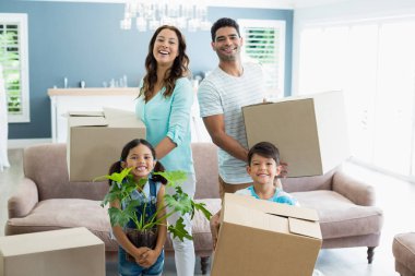 Parents and kids holding cardboard boxes in living room at home clipart
