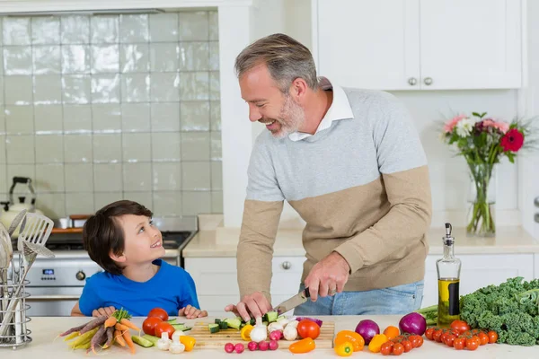 Батько взаємодіє з сином, нарізаючи огірок на дошці на кухні — стокове фото