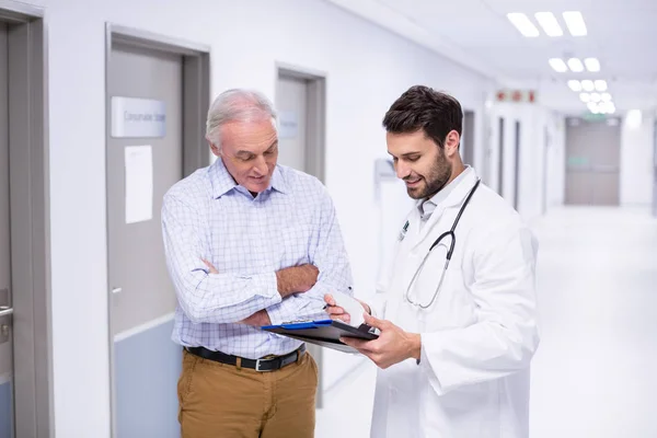 Arzt und Patient diskutieren auf Klemmbrett im Flur — Stockfoto