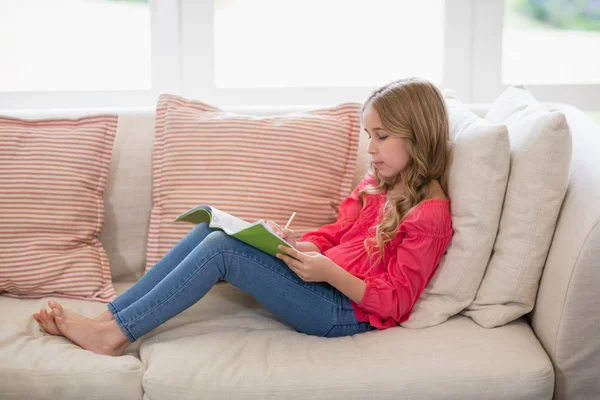 Tjejen sitter på soffan och göra läxor i vardagsrum — Stockfoto