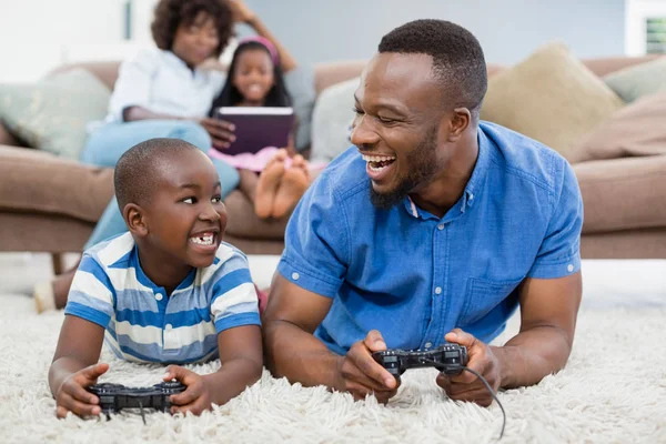 Отец и сын лежат на ковре и играют в видеоигры — стоковое фото