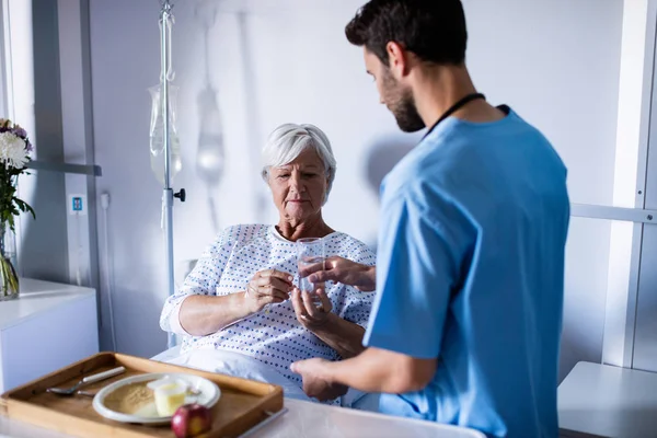 Doctor serving medicine to female senior patient on bed — Stock Photo, Image