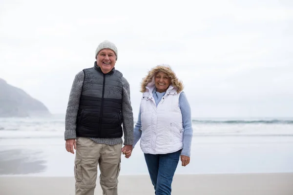 Старшая пара, идущая с поднятыми руками по пляжу — стоковое фото