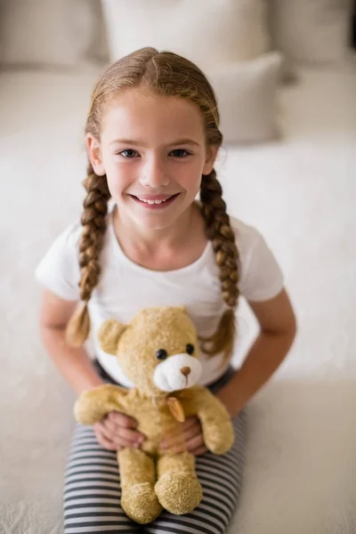 Chica sosteniendo un oso de peluche en la cama en el dormitorio — Foto de Stock