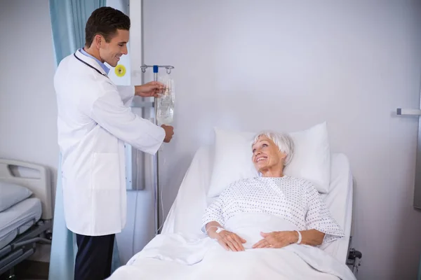 Arzt reguliert Tropf, während Patient auf Bett liegt — Stockfoto