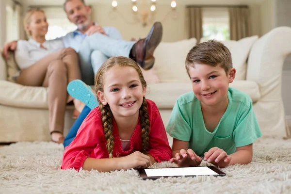 Rodzeństwo, leżąc na dywanie i za pomocą cyfrowego tabletu w salonie — Zdjęcie stockowe