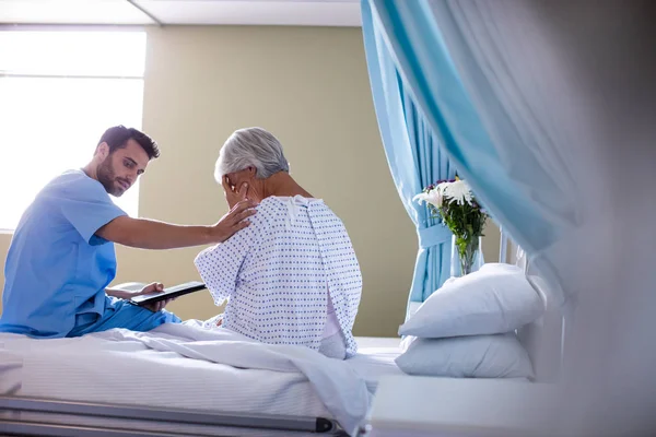 Врач-мужчина утешает пожилого пациента на кровати — стоковое фото