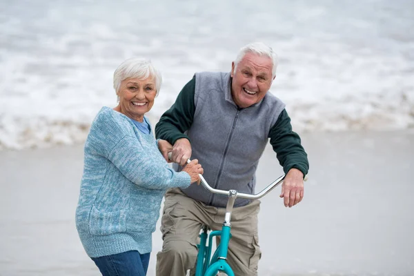 Senior paar staande met fietsen op het strand — Stockfoto