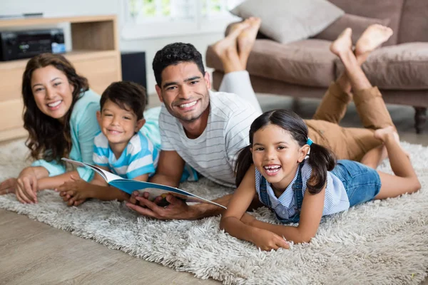 Retrato de padres e hijos acostados sobre una alfombra y leyendo un libro —  Fotos de Stock