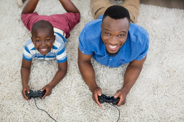 Портрет отца и сына, лежащих на ковре и играющих в видеоигры — стоковое фото