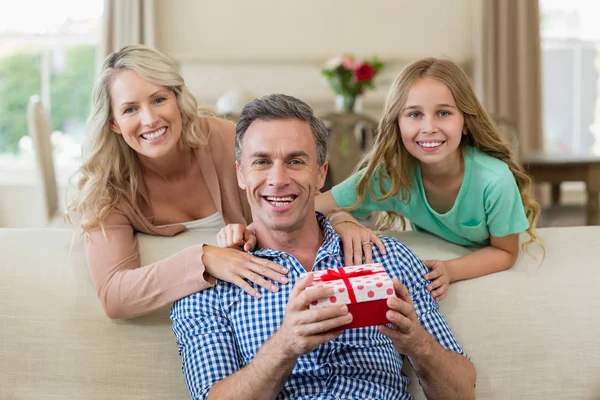 Father receiving a gift from his daughter and wife in living room — Stock Photo, Image