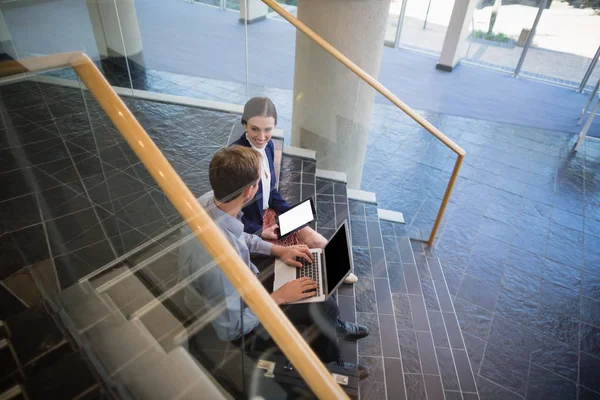 Businessman and woman sitting on steps using laptop and digital tablet — Stock Photo, Image
