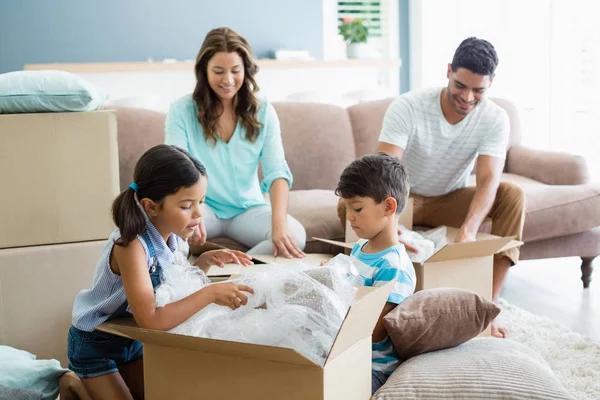 Pais e crianças desembalando caixas de papelão na sala de estar — Fotografia de Stock