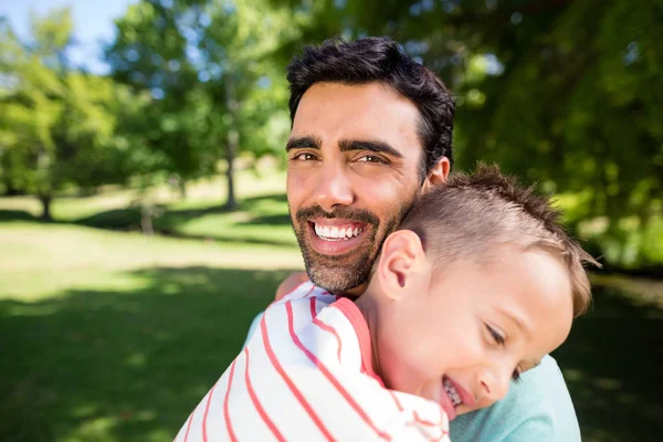Vater lächelt, während er seinen Sohn im Park umarmt — Stockfoto