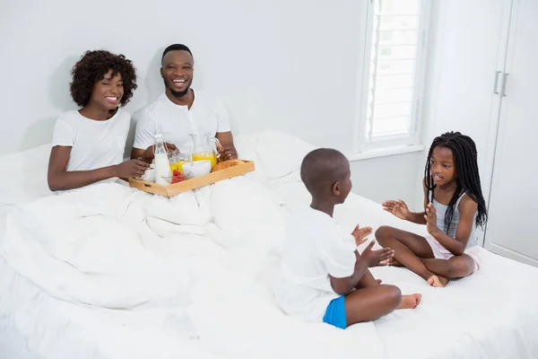 Niños divirtiéndose en el dormitorio mientras los padres desayunan en segundo plano —  Fotos de Stock