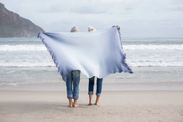 Coppia matura tenendo scialle dietro la schiena sulla spiaggia — Foto Stock
