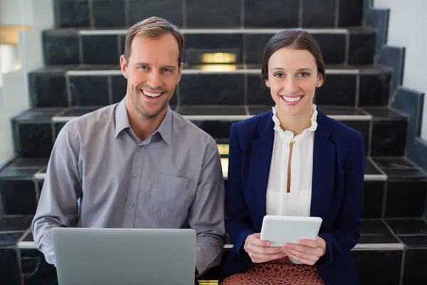Бизнесмен и женщина сидят на ступеньках, держа ноутбук — стоковое фото