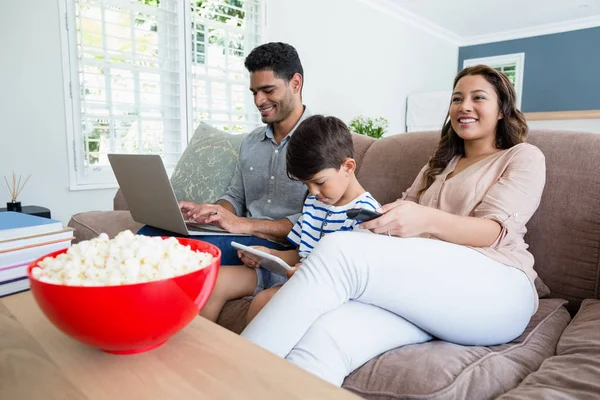 Madre viendo la televisión mientras padre e hijo usando portátil y tableta digital — Foto de Stock