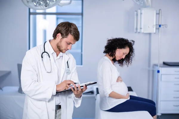 Arzt liest Klemmbrett bei Untersuchung von Schwangerer — Stockfoto