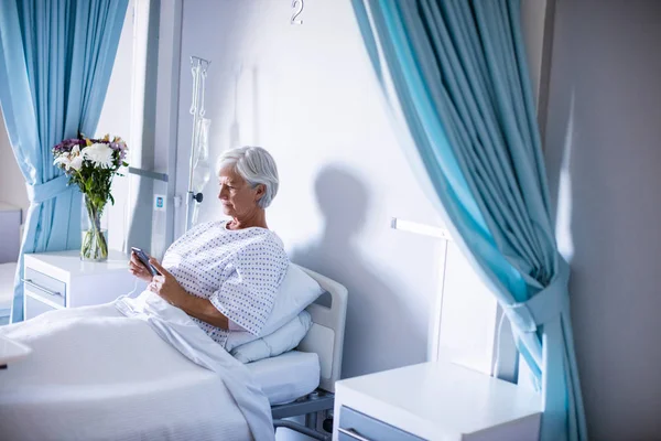 Paciente mayor femenina usando teléfono móvil en la cama —  Fotos de Stock