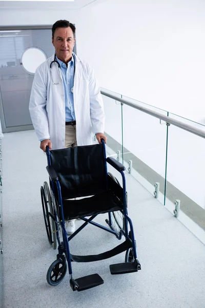 Médico varón empujando una silla de ruedas vacía en el pasillo —  Fotos de Stock