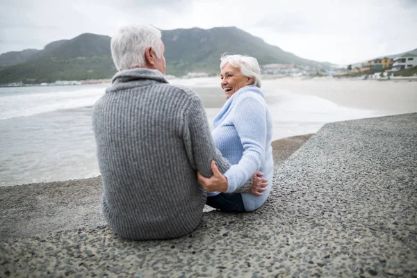 Старшая пара, сидящая на скале на пляже — стоковое фото