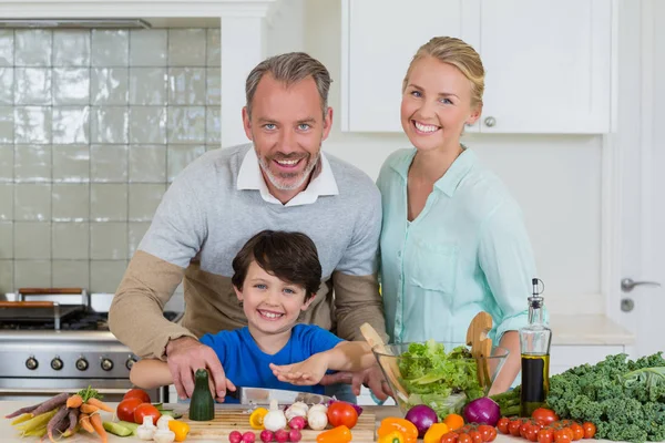Улыбающиеся родители и сын рубят овощи на кухне — стоковое фото