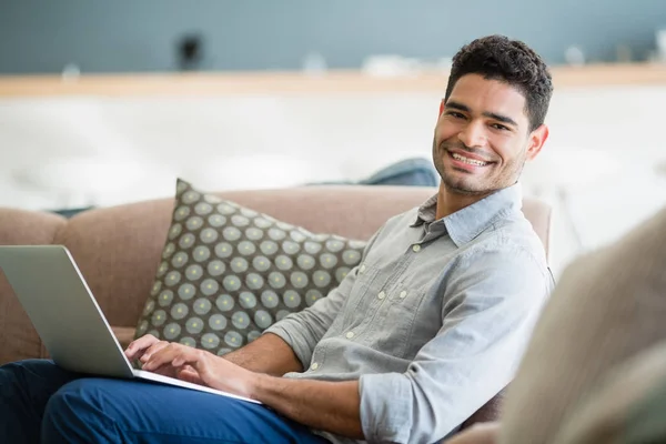 Man sitter på soffan och använder bärbar dator i vardagsrummet hemma — Stockfoto