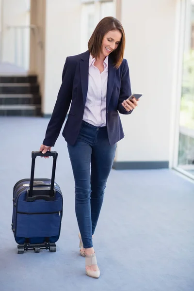 Businesswoman carrying luggage and using mobile phone — Stock Photo, Image