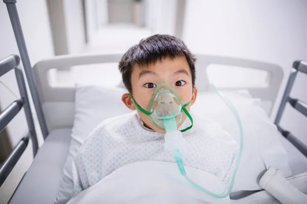 Boy patient wearing oxygen mask lying on hospital bed — Stock Photo, Image