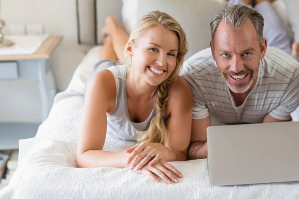 Sorrindo casal deitado na cama com laptop no quarto — Fotografia de Stock