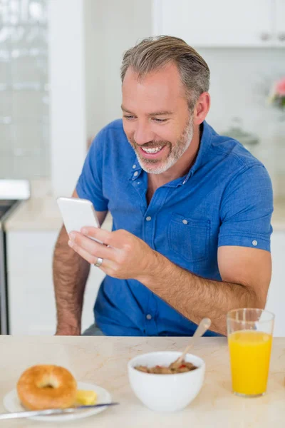 Mutfakta Kahvaltı yaparken cep telefonu kullanan adam — Stok fotoğraf